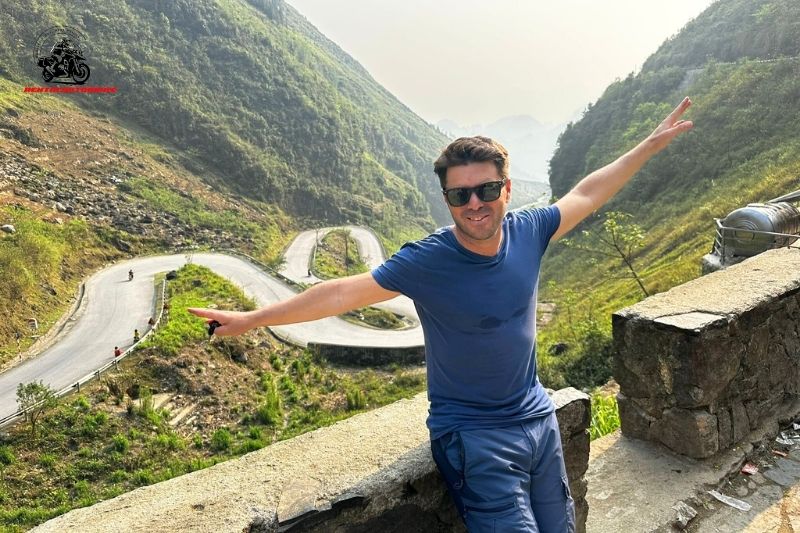 A man posing with arms outstretched on a mountain road