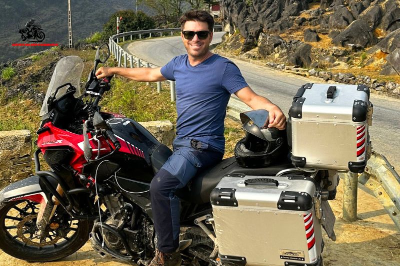 A man sitting on a bike, with luggage attached, on a mountain road