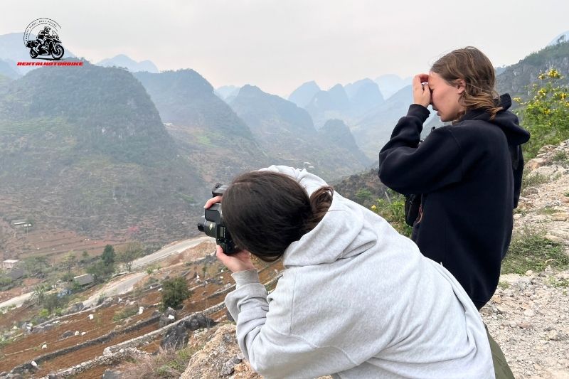 Two female travelers taking photos of Ha Giang mountains