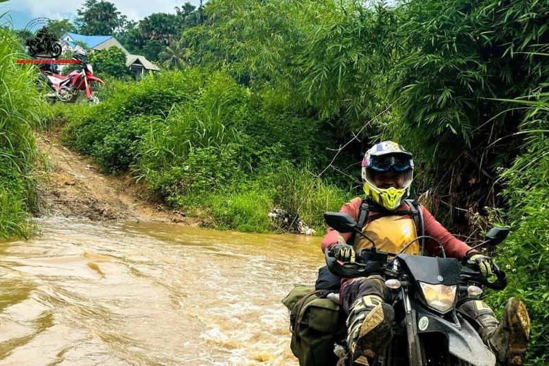 Motorbike rider crossing muddy stream in Vietnam jungle trail