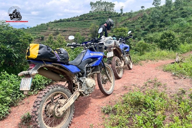 Dirt bikes parked on red soil trail with rider adjusting gear