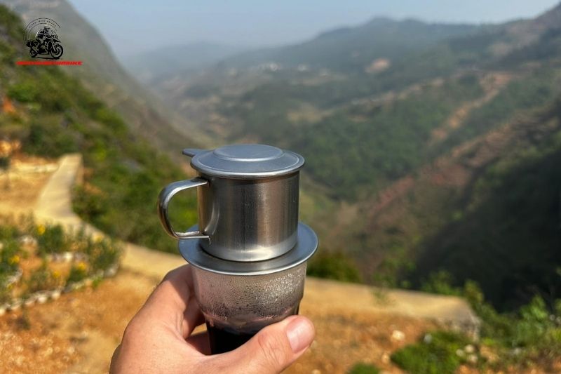 Hand holding drip coffee in front of mountain view