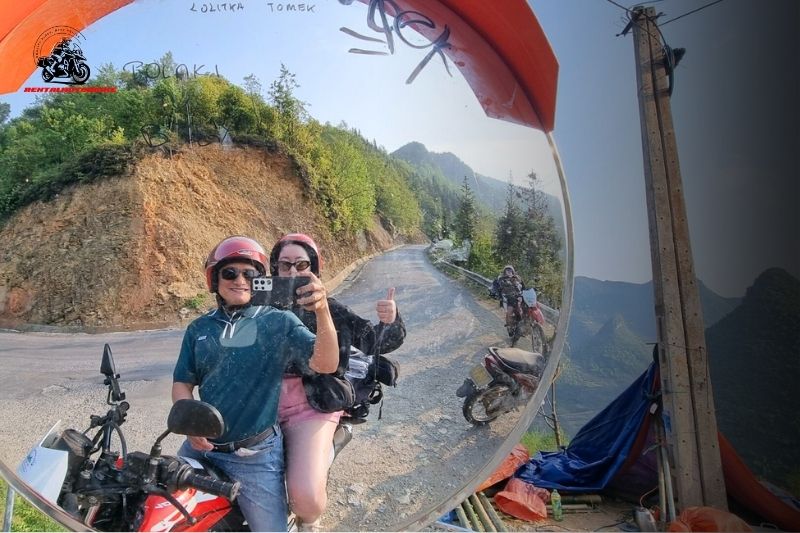Couple taking a mirror selfie on a motorbike with mountain road behind