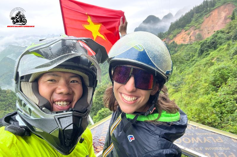 Two bikers smiling with helmets, holding a red Vietnamese flag