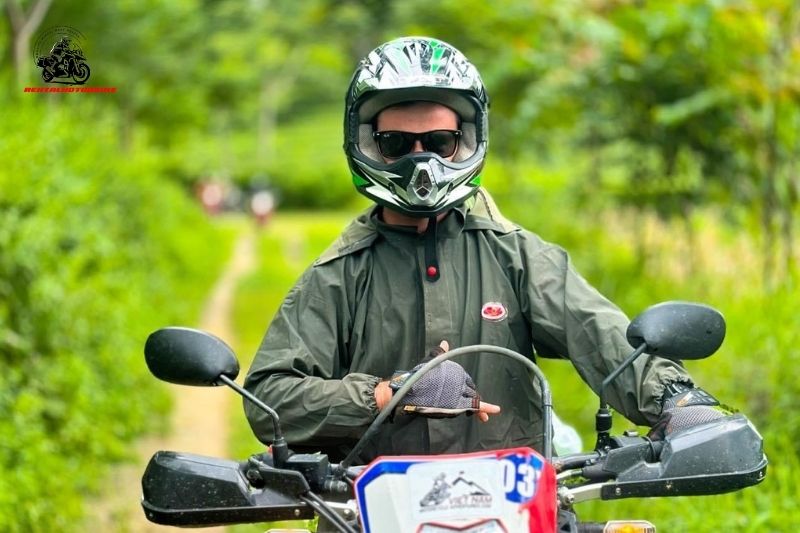 Biker in green jacket and helmet on a dirt path surrounded by forest