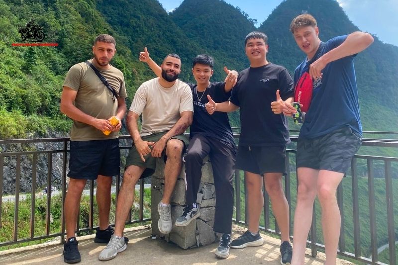 Five tourists smiling on a scenic mountain pass with green cliffs