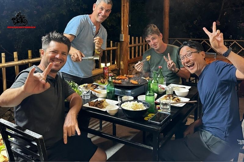Four men smiling and enjoying BBQ dinner together after a motorbike tour