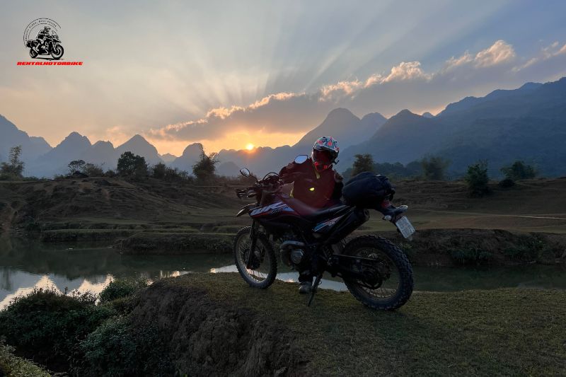 Biker with dirt bike watching sunset over mountain valley in Vietnam